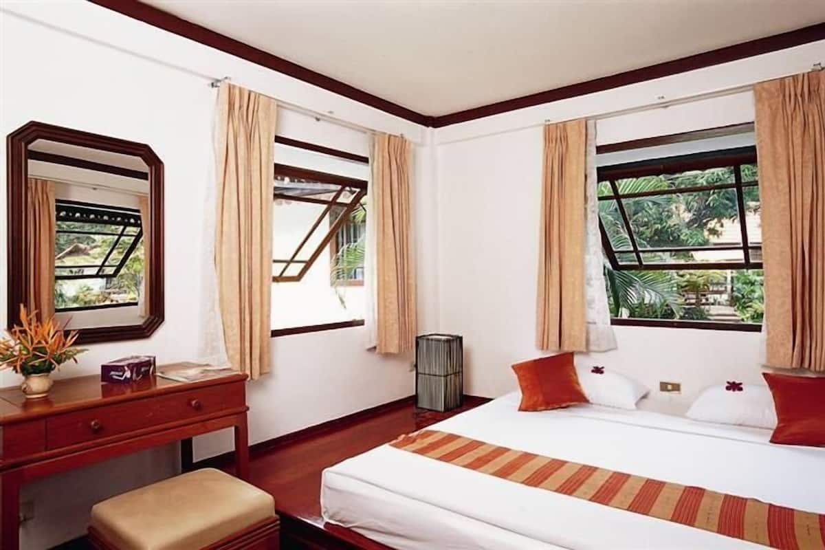 Una habitación de hotel con cama, escritorio, espejo y ventanas con cortinas.