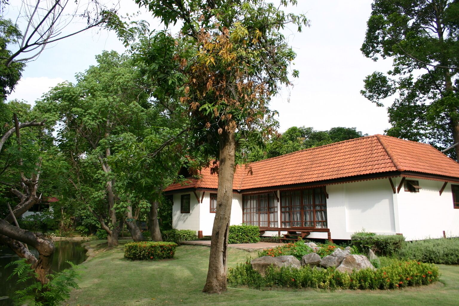 A traditional house with a tiled roof, surrounded by lush greenery and a pond.