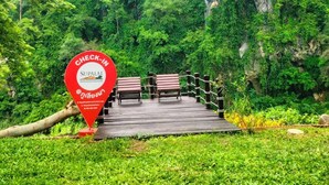 A check-in sign at Supalai with a wooden bridge leading to a seating area surrounded by lush greenery and a mountain backdrop. - Supalai Pasak Resort Hotel and Spa (Tha Khlo)
