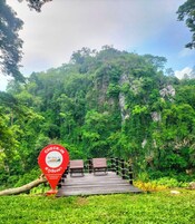 Señal de recepción en Supalai, con un puente de madera que conduce a una zona de estar rodeada de abundante vegetación y un telón de fondo montañoso.