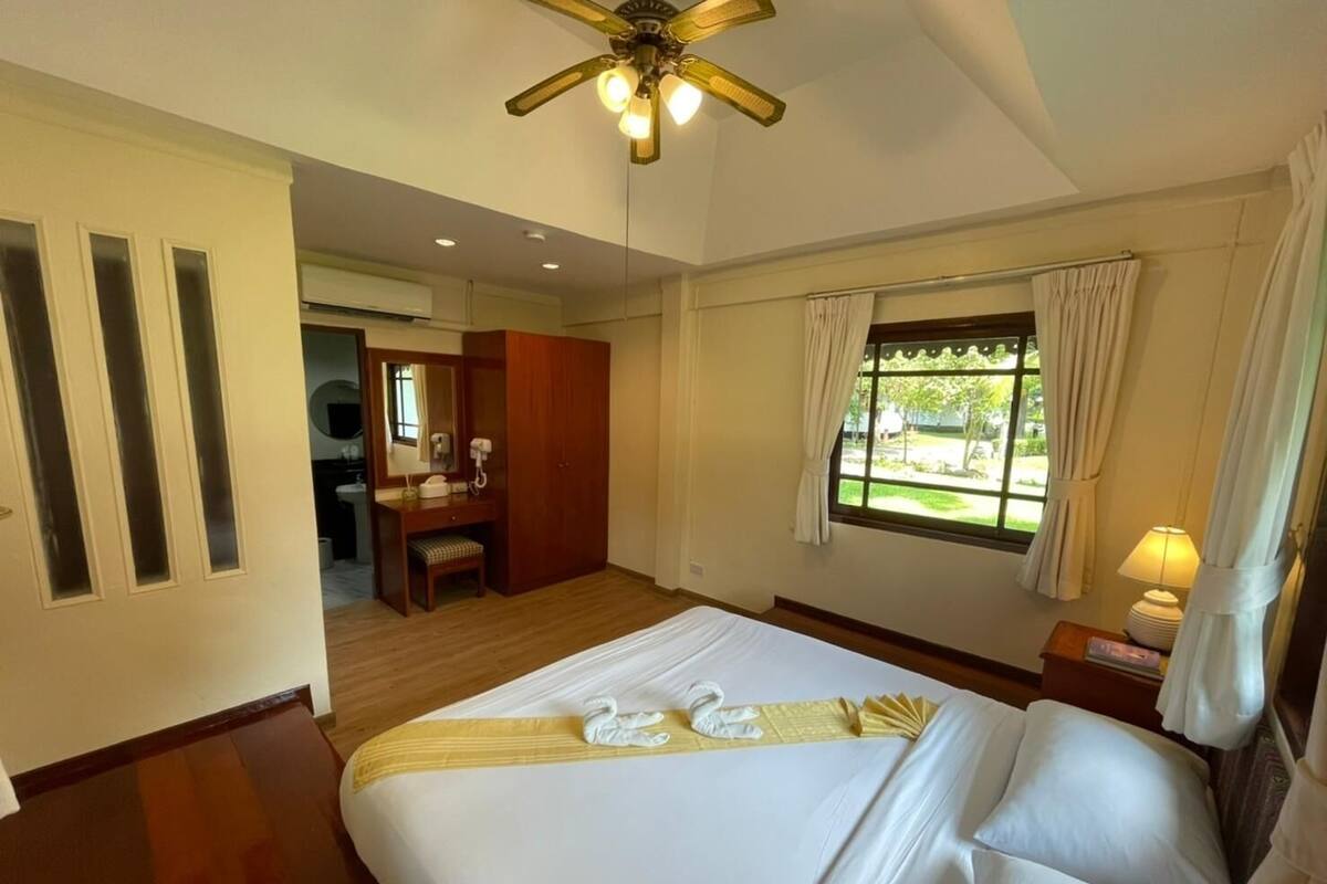 Habitación de hotel con una cama grande, un escritorio, una silla, un tocador con espejo y una ventana con cortinas.