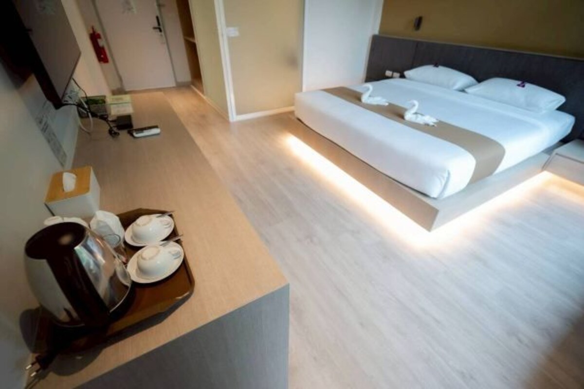 Una habitación de hotel moderna con una cama grande, mesitas de noche y una bandeja con cafetera y tazas.