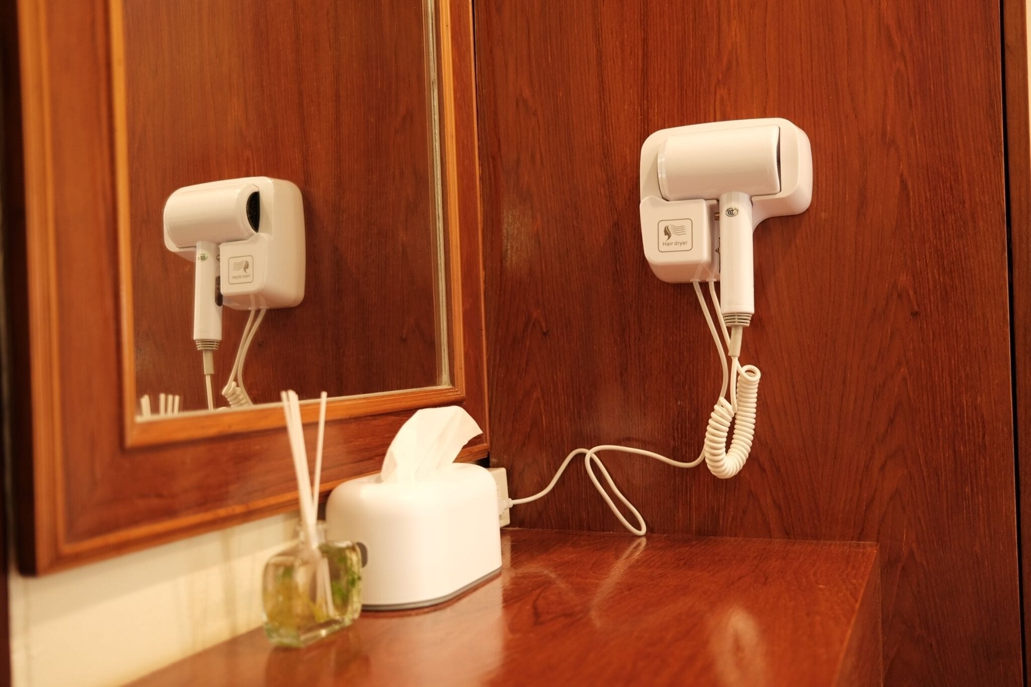 A hair dryer and a tissue box on a wooden counter in a bathroom.