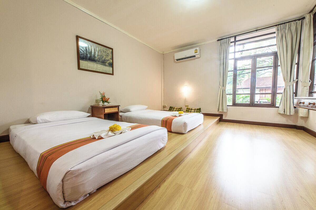 Habitación de hotel con dos camas, una mesita de noche con lámpara, un cuadro en la pared y una ventana con cortinas.
