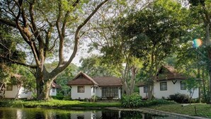 A serene lakeside setting with three white buildings, each with a brown roof, surrounded by lush greenery and trees. - Supalai Pasak Resort Hotel and Spa (Tha Khlo)