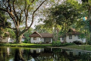 Un entorno tranquilo junto al lago, con tres edificios blancos, cada uno con techo marrón, rodeados de exuberante vegetación y árboles.