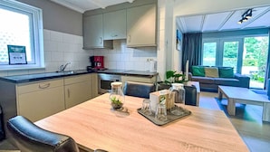 A modern kitchen with a dining area, featuring a wooden table, chairs, and a coffee machine.