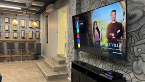 Ein modernes Wohnzimmer mit einem großen Flachbildfernseher an der Wand, einem Holztisch und einer Wand mit Muster.