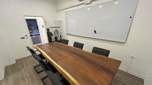 Ein Konferenzraum mit einem langen Holztisch, sechs Stühlen, einer Whiteboard-Tafel und einer Tür zu einem weiteren Raum.