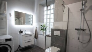 Un baño moderno con cabina de ducha de vidrio, un lavabo blanco y una lavadora integrada.