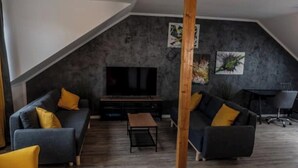 A modern living room with a sloped ceiling, a flat-screen TV, two sofas with yellow cushions, and a wooden column.
