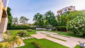 A modern building with a courtyard featuring a well-maintained lawn, stone pathways, and various plants. - Cherry Villa,Nashik by Ebony Stays | Cosy 4BHK Villa in Nashik with Scenic Views (Nashik)