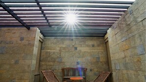 A sunlit room with stone walls, two wooden chairs, and a small table. - Cherry Villa,Nashik by Ebony Stays | Cosy 4BHK Villa in Nashik with Scenic Views (Nashik)