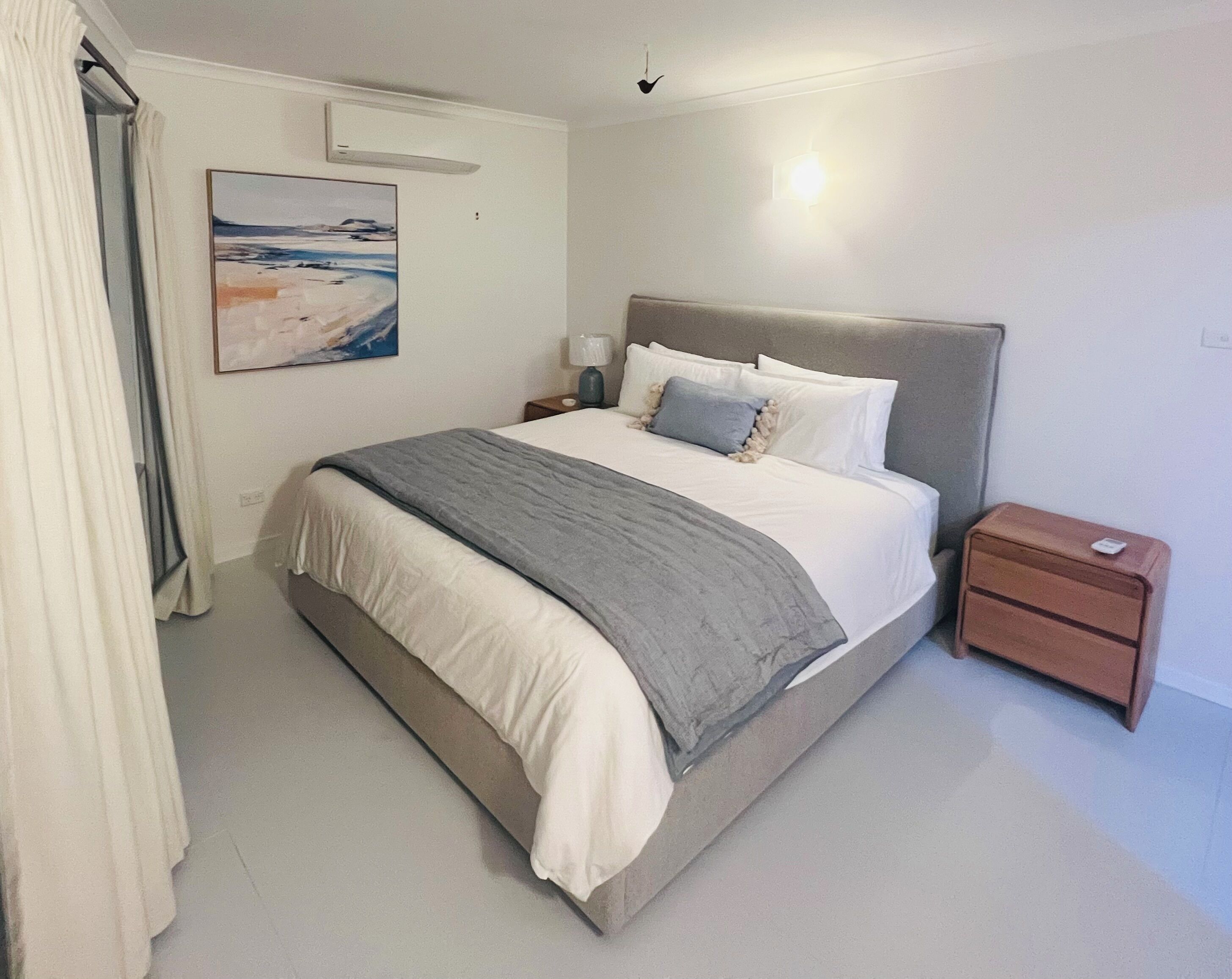 A neatly arranged bedroom with a bed, bedside tables, a lamp, and a painting on the wall.