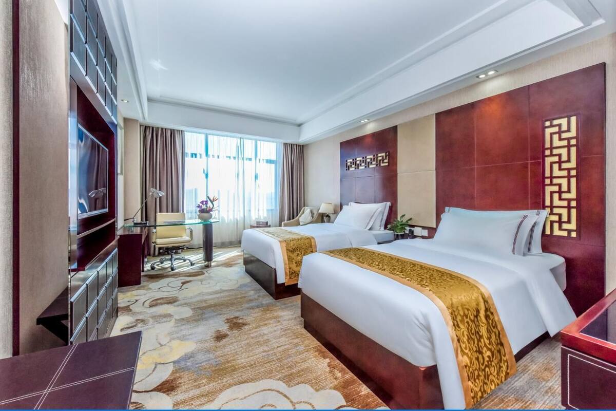 Une chambre d’hôtel avec deux lits, un bureau, une télévision et une grande fenêtre avec des rideaux.