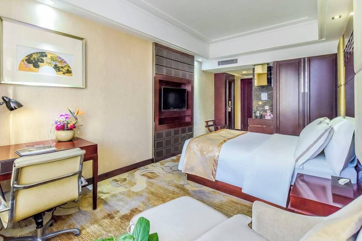 Une chambre d’hôtel comprenant un lit, un bureau avec une chaise, une télévision et une petite table sur laquelle est posé un vase de fleurs.