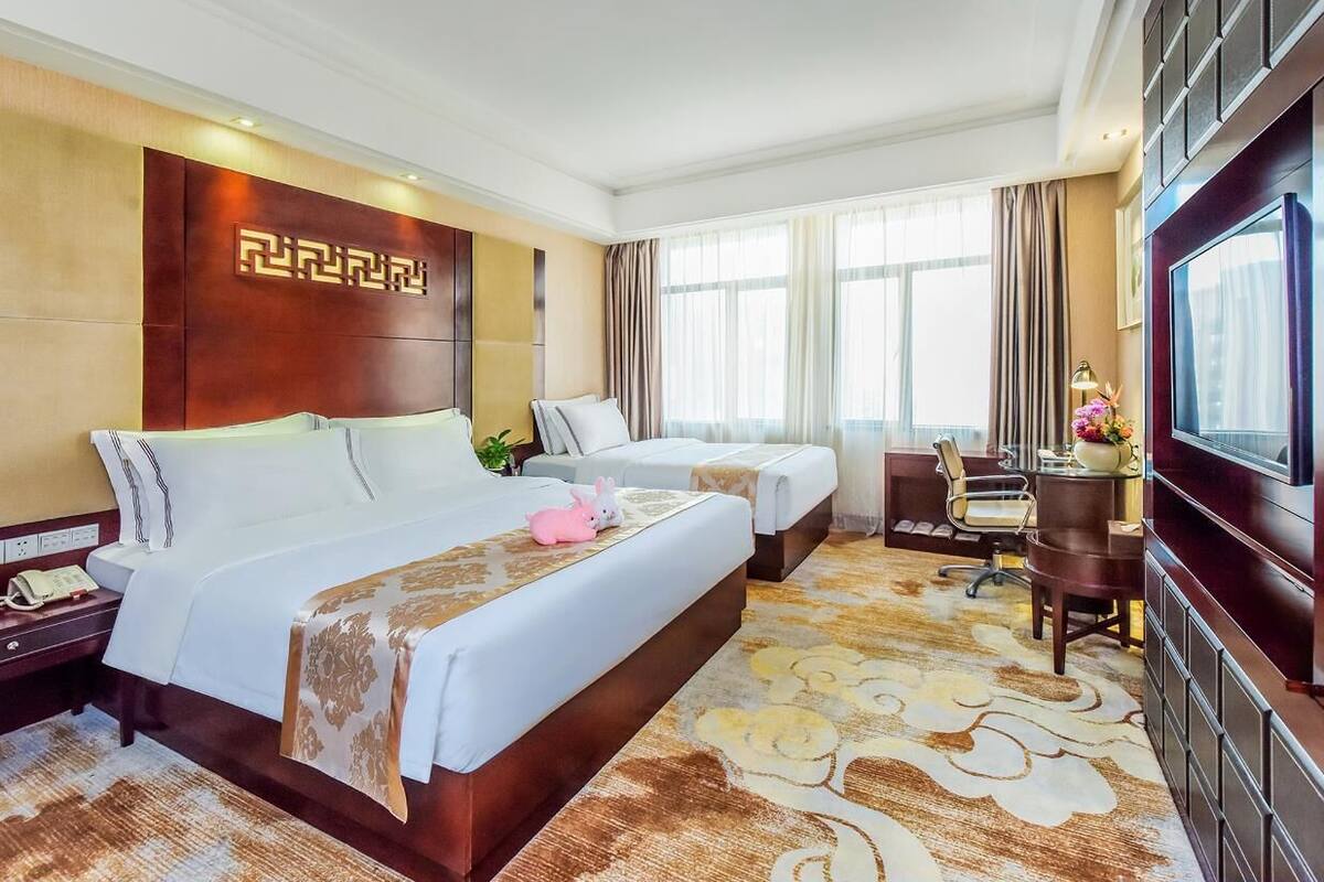 Une chambre d’hôtel avec deux lits, un bureau, une chaise, une télévision et une grande fenêtre avec des rideaux.