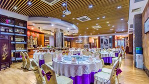 A banquet hall with round tables set for a formal event, featuring white tablecloths and gold chairs with purple sashes.