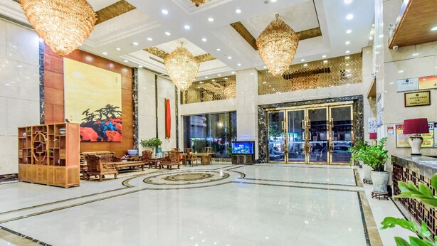 A spacious lobby with chandeliers, a reception desk, and a large painting on the wall.