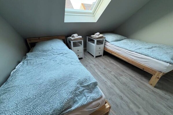 A small, cozy room with two single beds, a skylight, and a wooden floor.