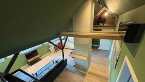Ein Zimmer mit hohen Decken, einer Holztreppe, einem Flachbildfernseher und einer kleinen Sitzecke.