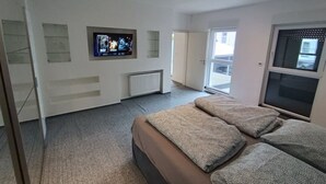 Ein modernes Schlafzimmer mit einem großen Bett, einem an der Wand befestigten Fernseher und einer Glastür, die auf einen Balkon führt.