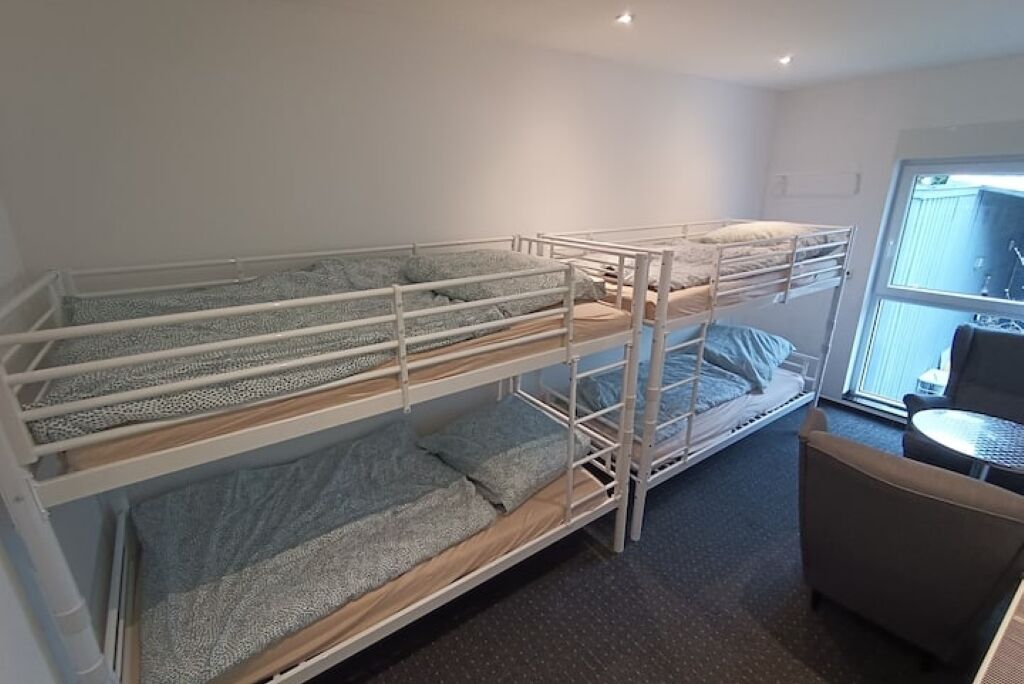 A bunk bed room with a small table and chair, a window with blinds, and a door leading outside.