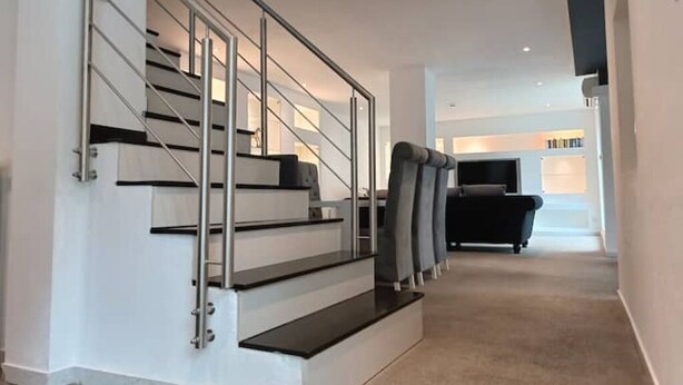 Eine moderne Treppe mit Metallgeländern und Teppichboden, die zu einem Wohnbereich mit einem schwarzen Sofa und einem Flachbildfernseher führt.