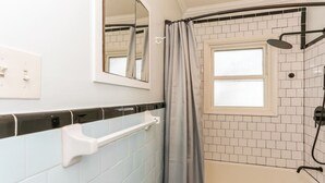 A bathroom with a bathtub, a shower, a window, and a handrail.
