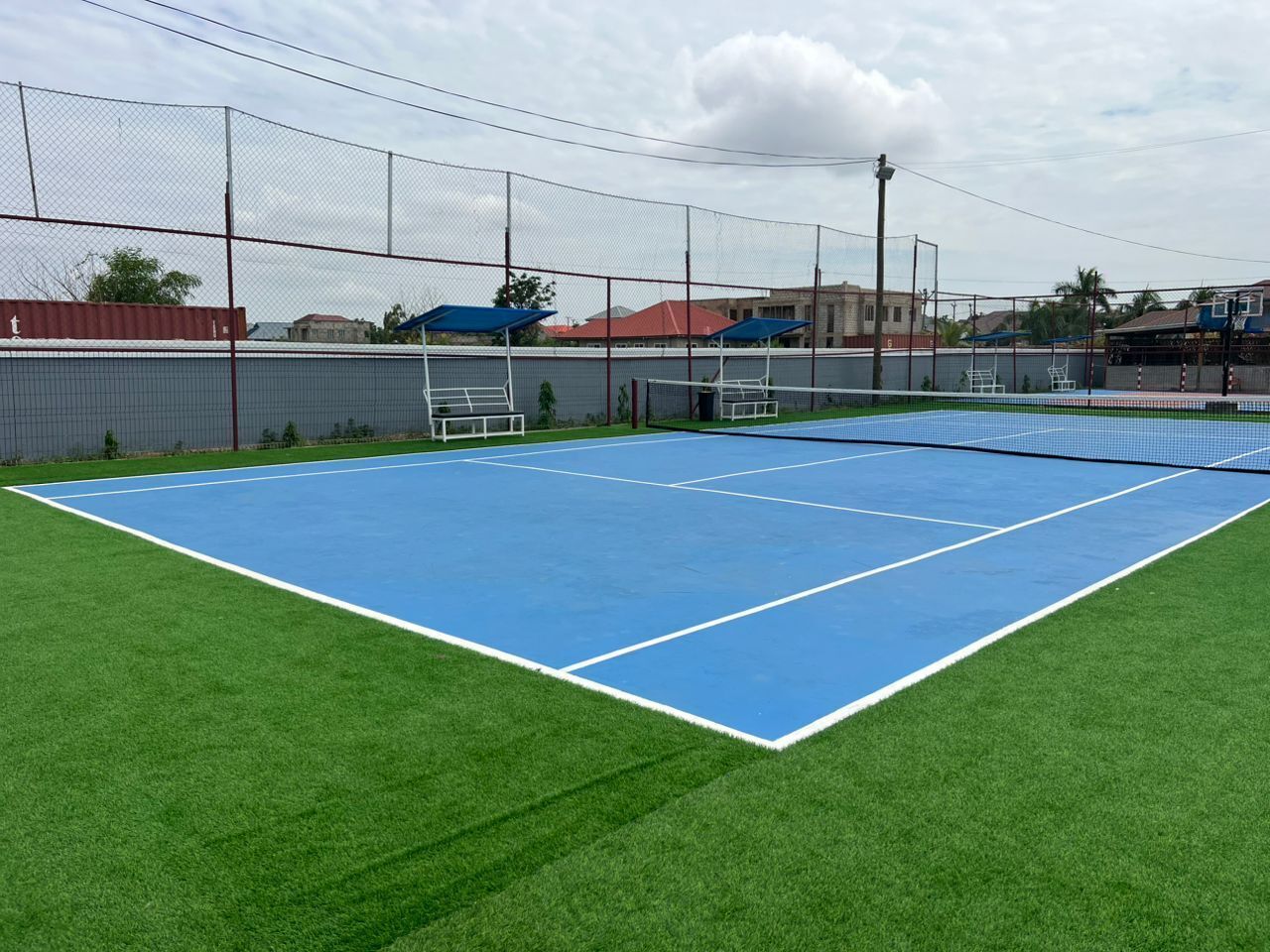 Ein Tennisplatz mit Netz, umgeben von einem Zaun und einer Rasenfläche.