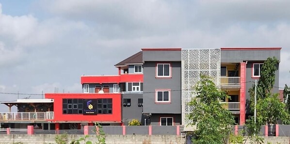 A multi-story building with a red and grey facade, balconies, and a patterned wall.