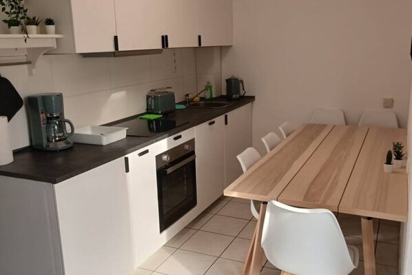 Cozinha compacta com armários brancos, cafeteira, torradeira e mesa de jantar de madeira com cadeiras.