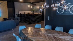 Un comedor moderno con una gran mesa de madera y sillas azules, una zona de bar con taburetes y una lámpara con motivos de bicicleta.