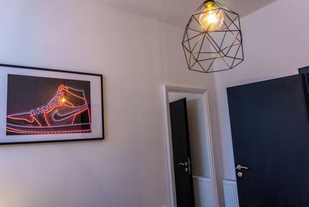 Una obra de arte en un marco en la pared, una lámpara con diseño geométrico y una puerta.