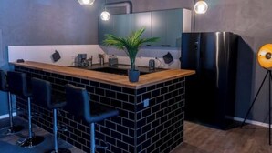 Una cocina moderna con una isla central, salpicadero de azulejos negros, taburetes de bar, un refrigerador e iluminación colgante.