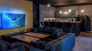 Una sala moderna con un televisor de pantalla plana grande, un sofá, una mesa de centro y una zona de cocina con encimera y electrodomésticos.