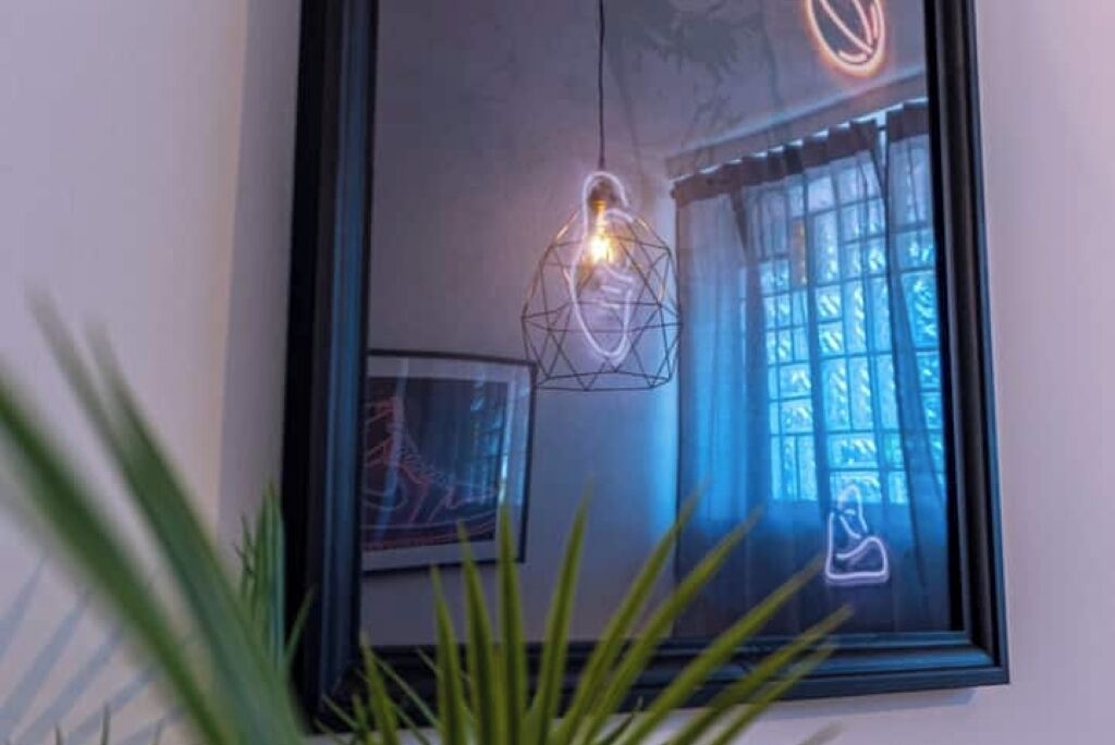 Uno specchio incorniciato che riflette una stanza con un lampadario dalle forme geometriche e una finestra con tende.