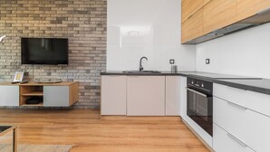 A modern kitchen with a brick wall, a flat-screen TV, and built-in appliances. - Jaglana Deluxe 2 by Grand Apartments (Gdansk)