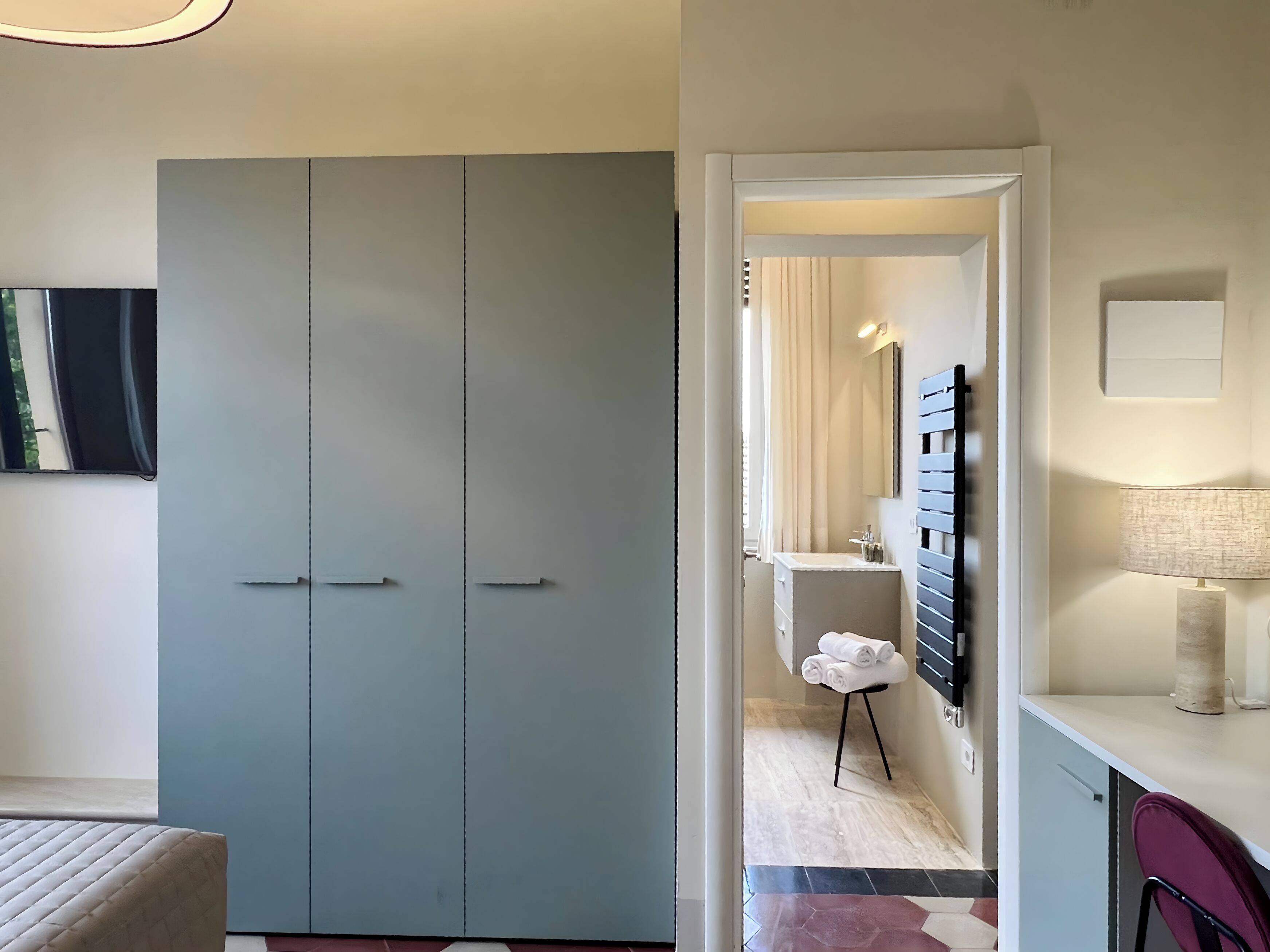 Un dormitorio moderno con un armario amplio, una cama y un baño que incluye un espejo, un lavabo y un perchero para toallas.
