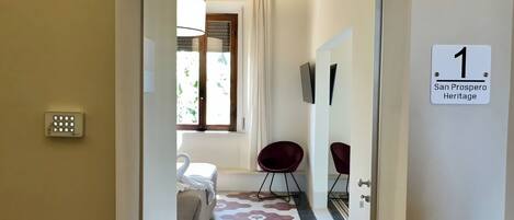 Un couloir doté d’un sol à motifs géométriques, un lit avec un oreiller en forme de cygne, une chaise rouge et un panneau indiquant le numéro de la chambre : 1.