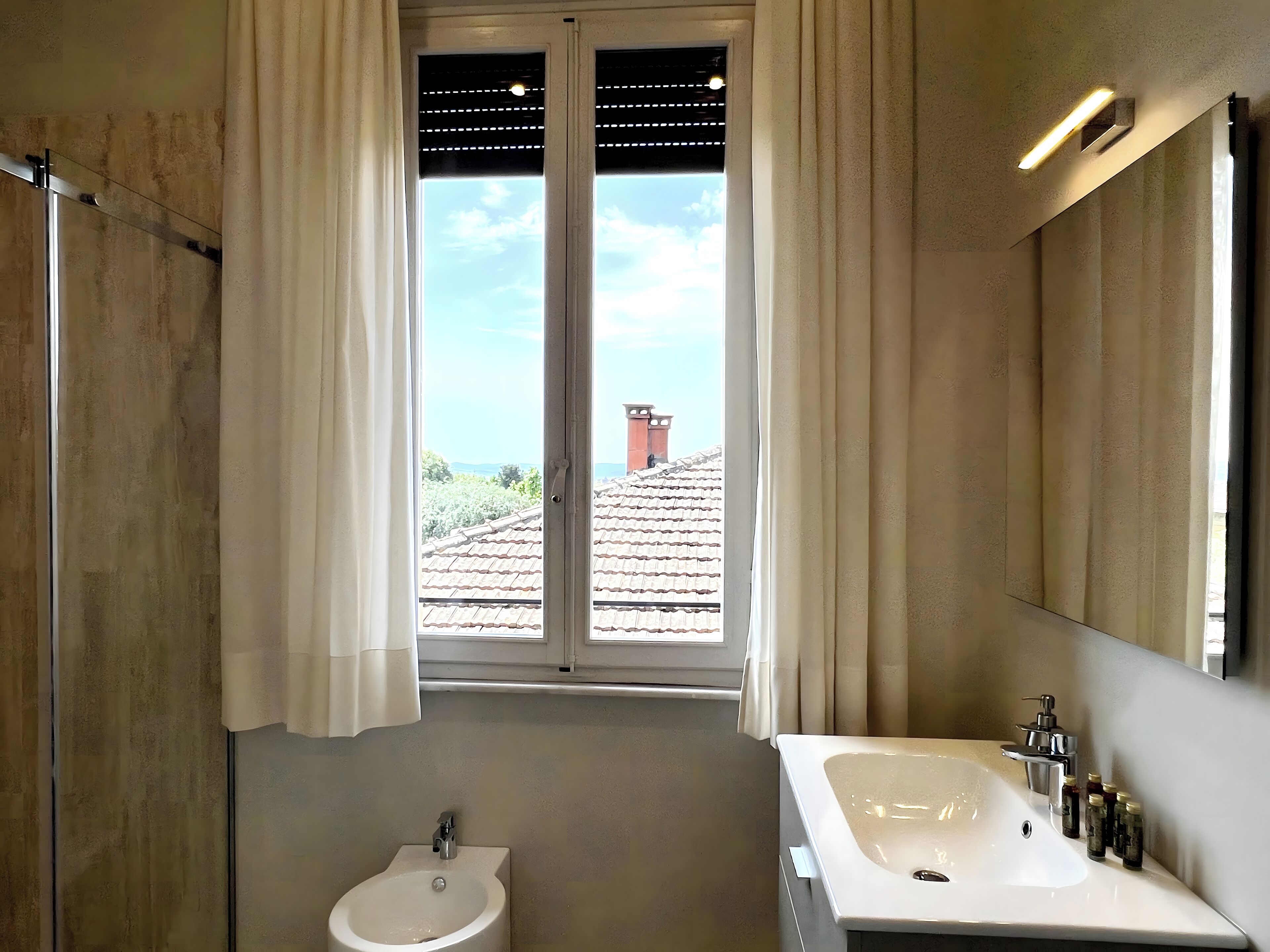 A bathroom with a large window, a sink, and a mirror.