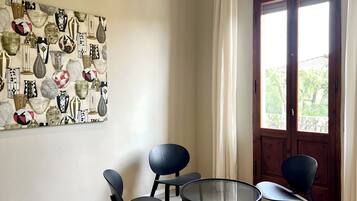 Una stanza con un affresco raffigurante diversi vasi, una porta in legno che dà su un balcone e un tavolo rotondo in vetro con quattro sedie.