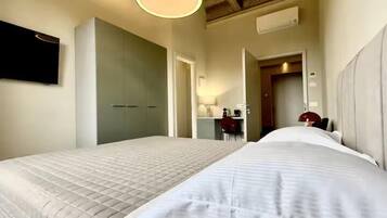 Habitación de hotel con dos camas, televisor montado en la pared, escritorio con silla y ventilador de techo.
