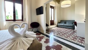 A hotel room with a bed, a sofa, a TV, and a dining area. - San Prospero Heritage (Siena)