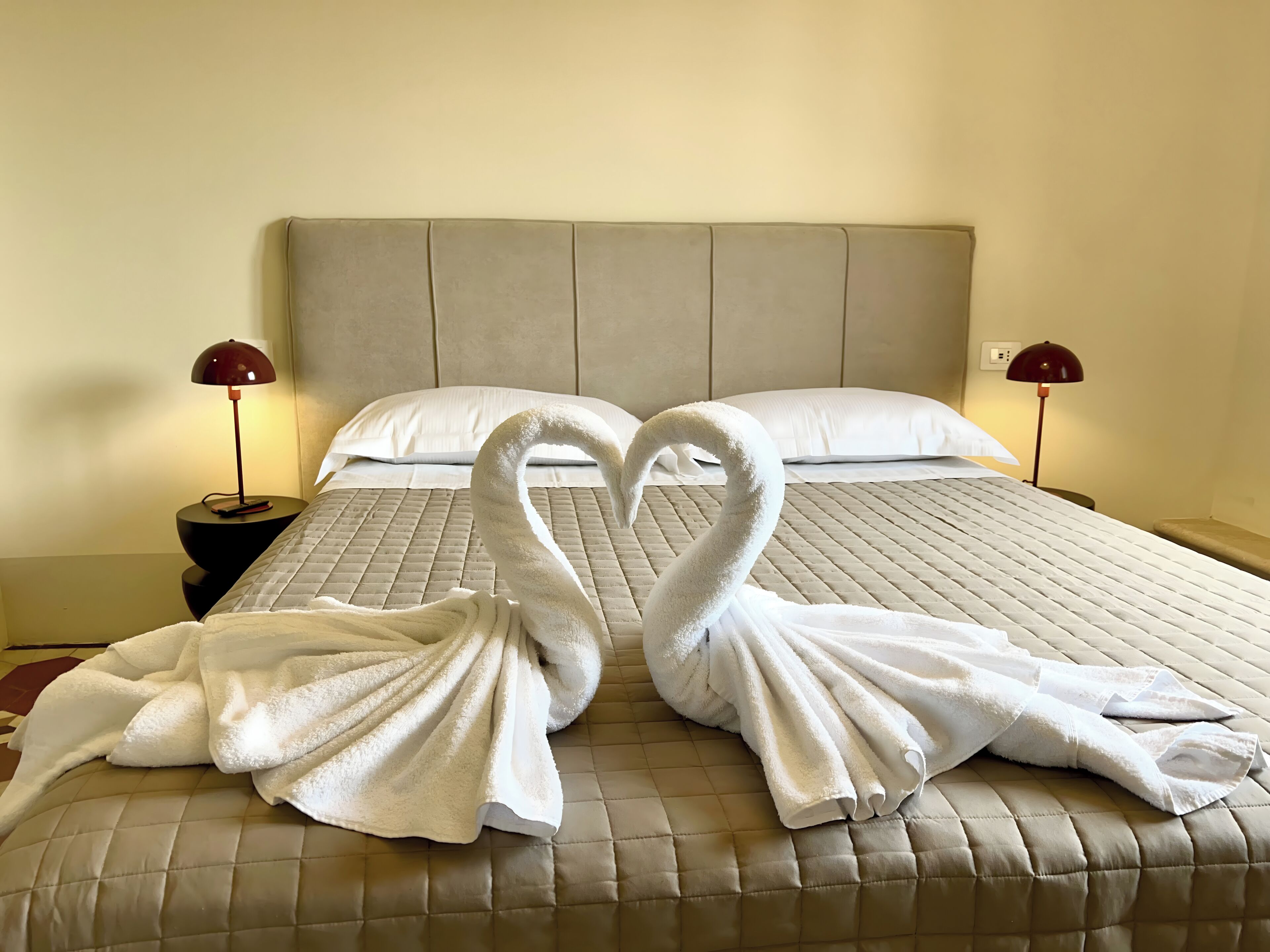 Un lit recouvert d’une courtepointe beige matelassée, avec deux oreillers blancs et deux lampes rouges de chaque côté.