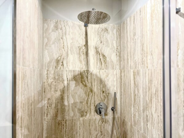 Ducha con cabezal de ducha tipo lluvia y cabezal de ducha de mano, ambos instalados en una pared de mármol.