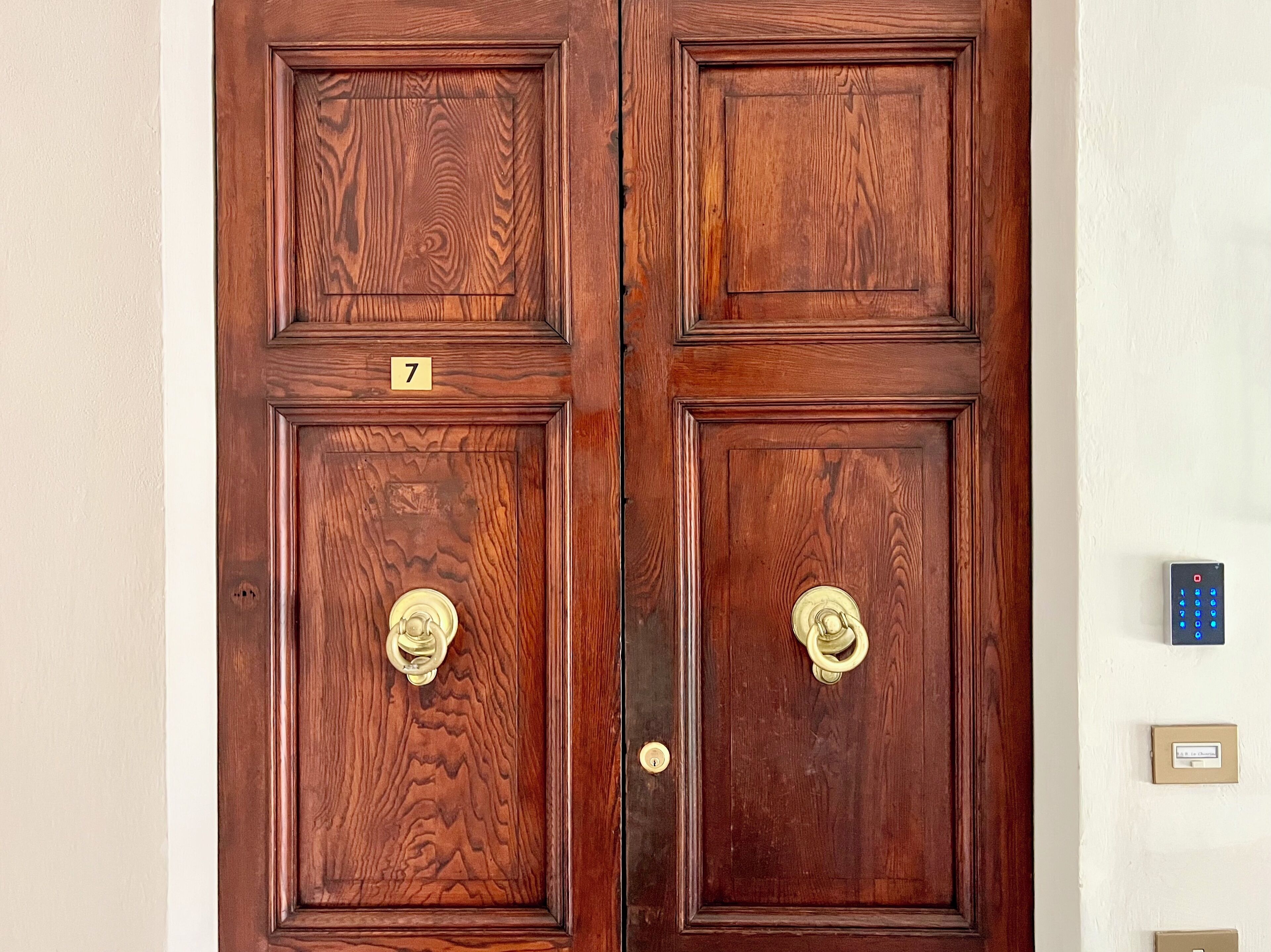 A wooden double door with brass handles and a number plate indicating room 7.