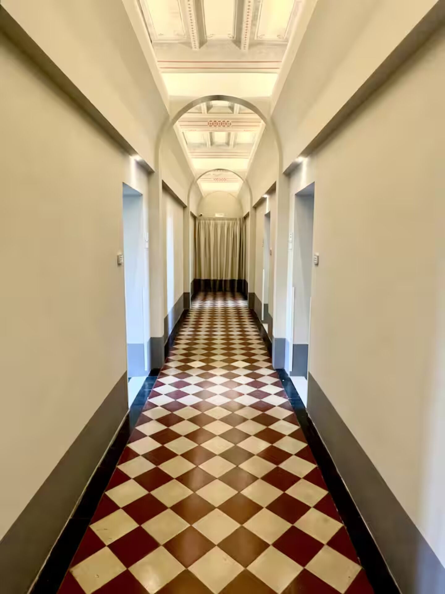 Un largo pasillo estrecho con piso a cuadros y un techo alto con molduras decorativas.