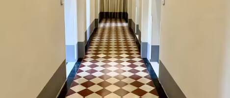 Un largo pasillo estrecho con piso a cuadros y un techo alto con molduras decorativas.