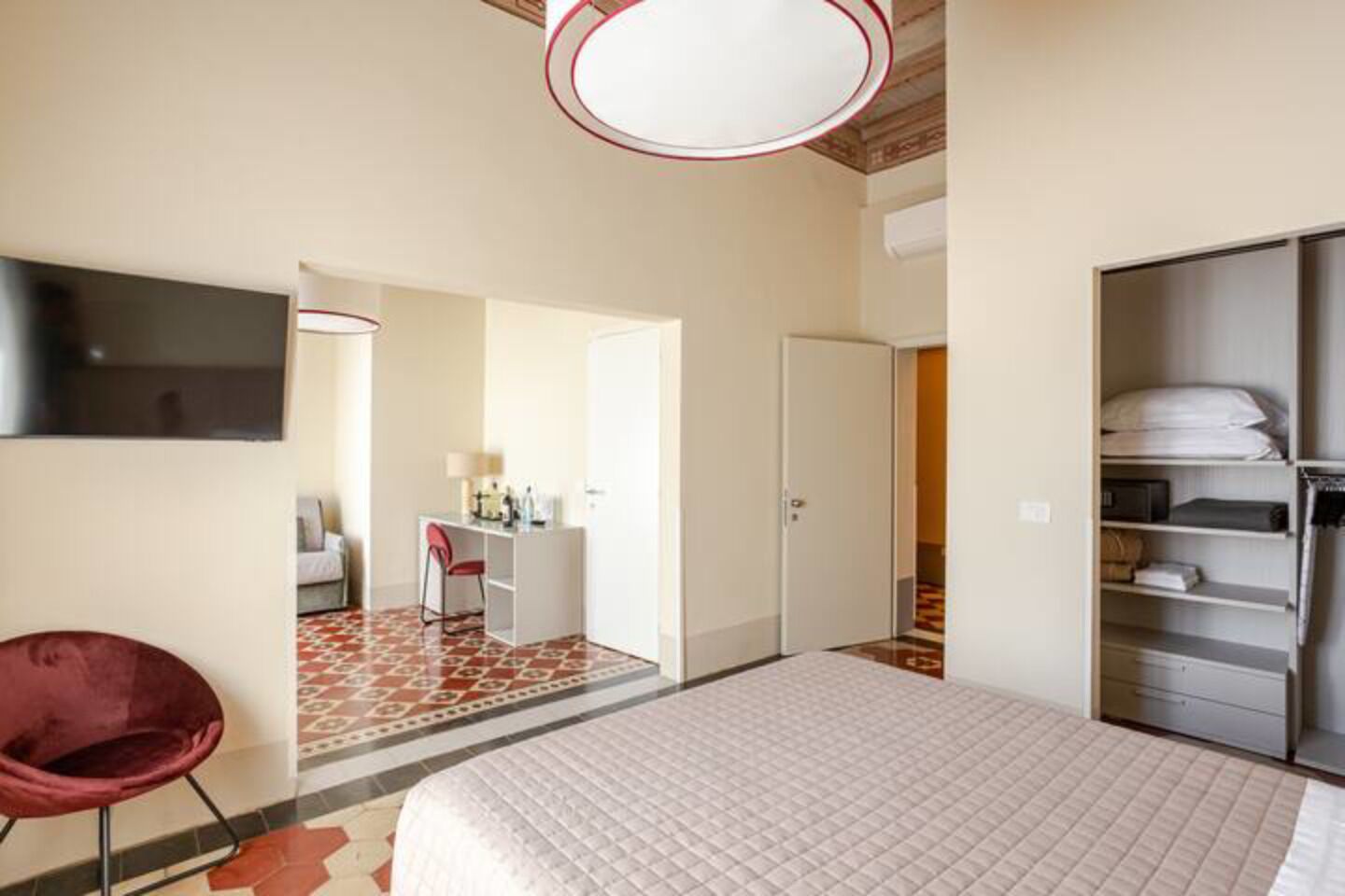 A hotel room with a bed, a desk with a chair, a wardrobe, and a TV on the wall.